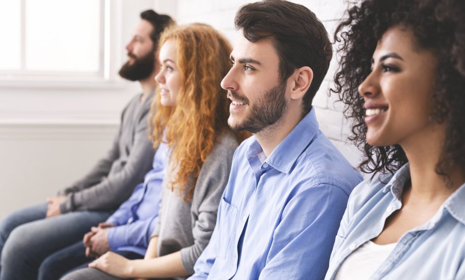 Multiethnic millennial people sitting in row and looking at something, waiting for speaker, attending group therapy session, side view
